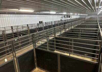 The inside of a barn arena with a lot of stalls.